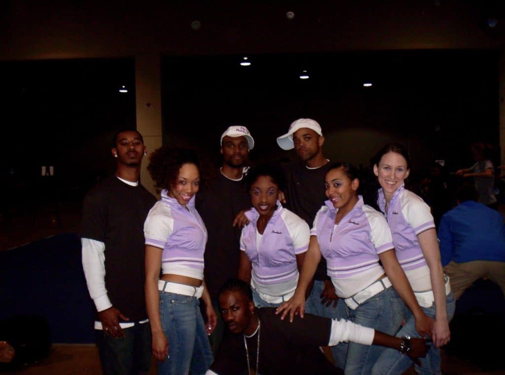 Photo of a hip hop team. Three young black men in the back row, 4 women in the middle row - 3 black, 1 white, one young black man kneeling down on the bottom row.