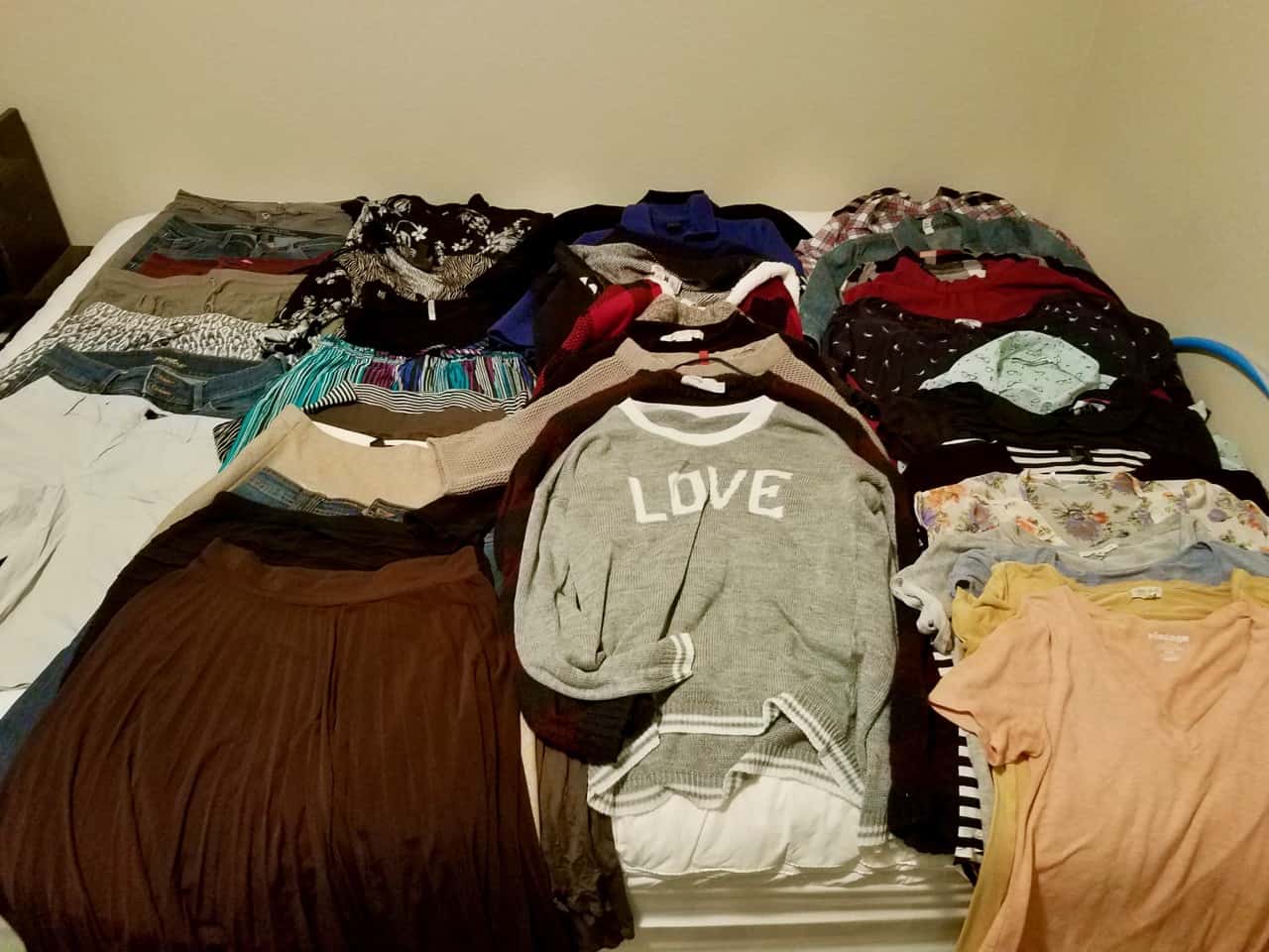 40 items of clothing, including shirts, sweaters, skirts, pants, laid out on a bed.