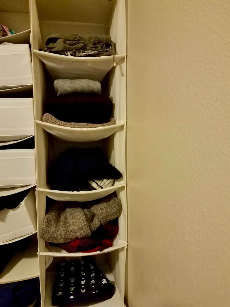 Pants and sweaters hanging in a shelf-like closet organizer.