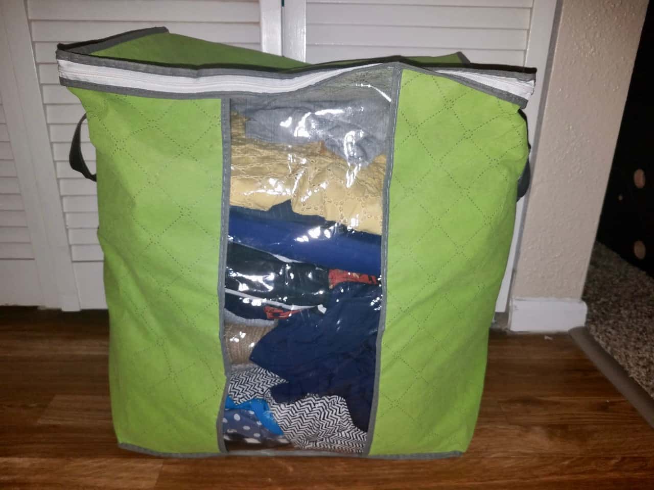 Green storage bag with a clear front so you can see all the clothing stored inside.