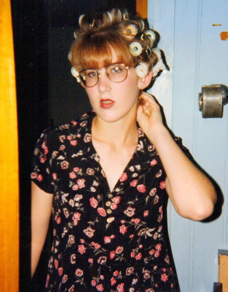 A photo of a caucasian teen girl with roller curlers in her hair, wearing a black dress with small pink flowers on it.