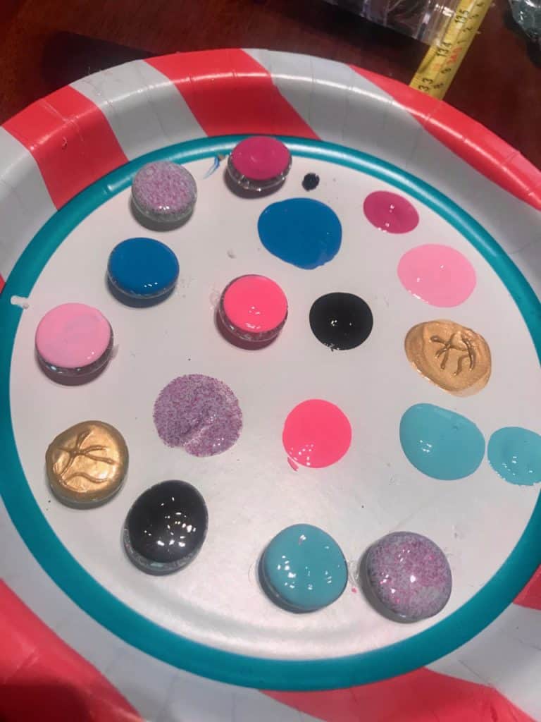 Flat glass marbles on a paper plate with the backsides painted in different colors.