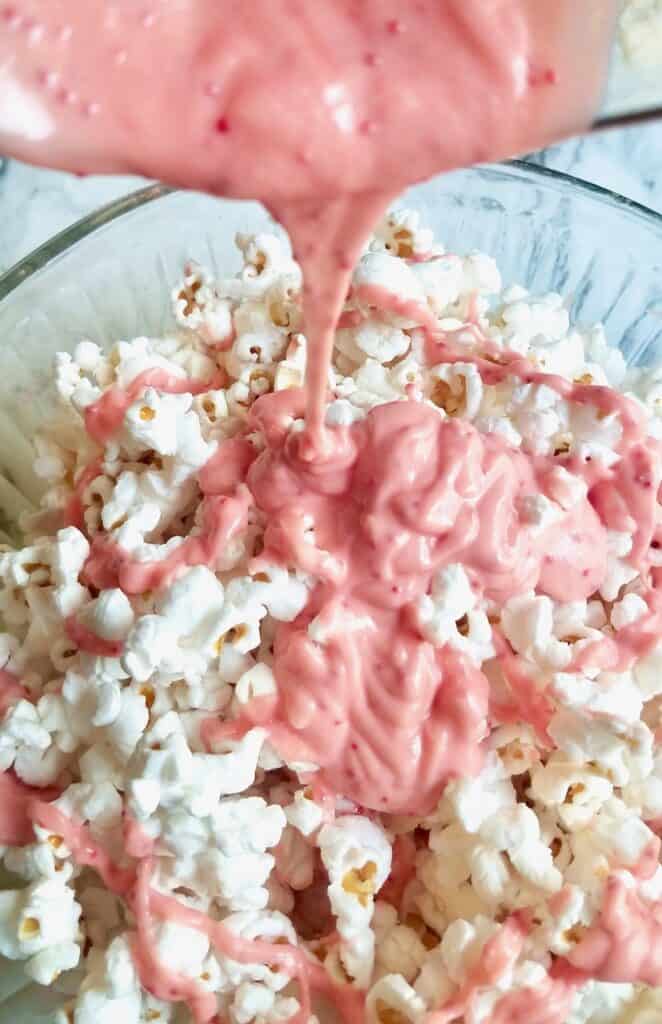 Pink white chocolate and peppermint melt being poured over popcorn