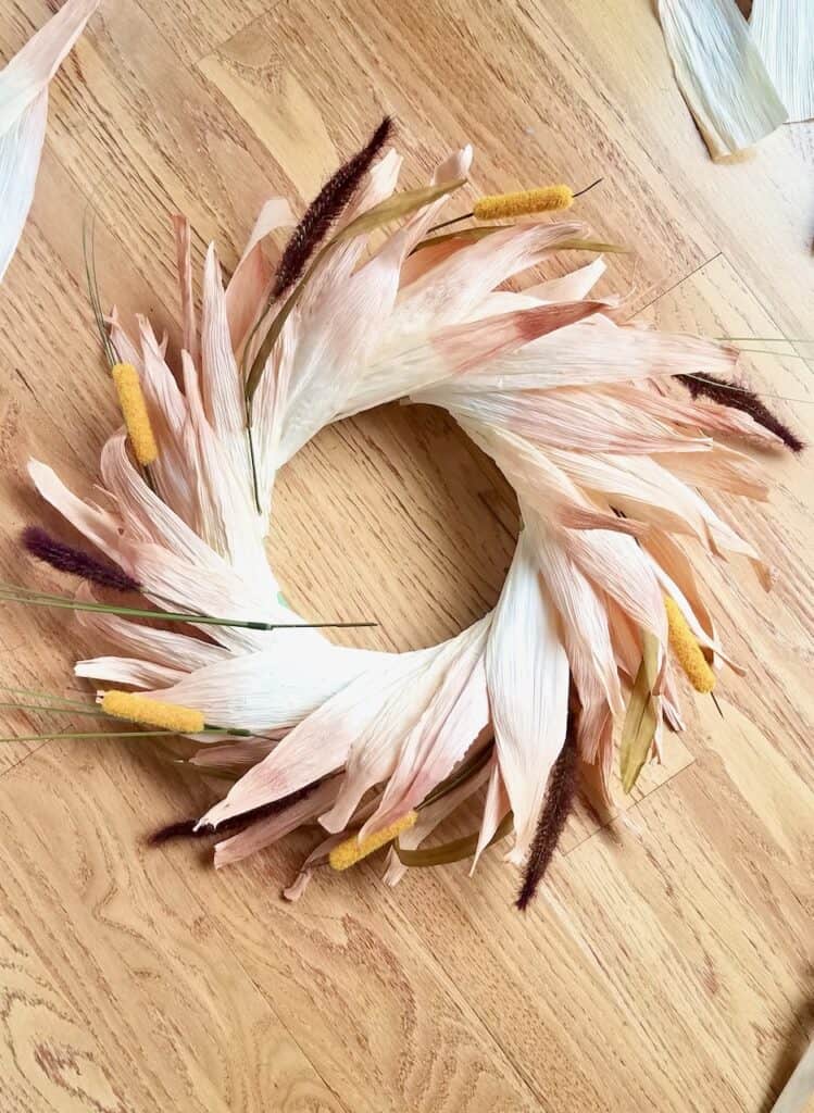 Adding fall floral into your corn husk wreath is a great way to add more pops of color. Learn how to make your own colorful corn husk wreath by following this tutorial. | We Three Shanes