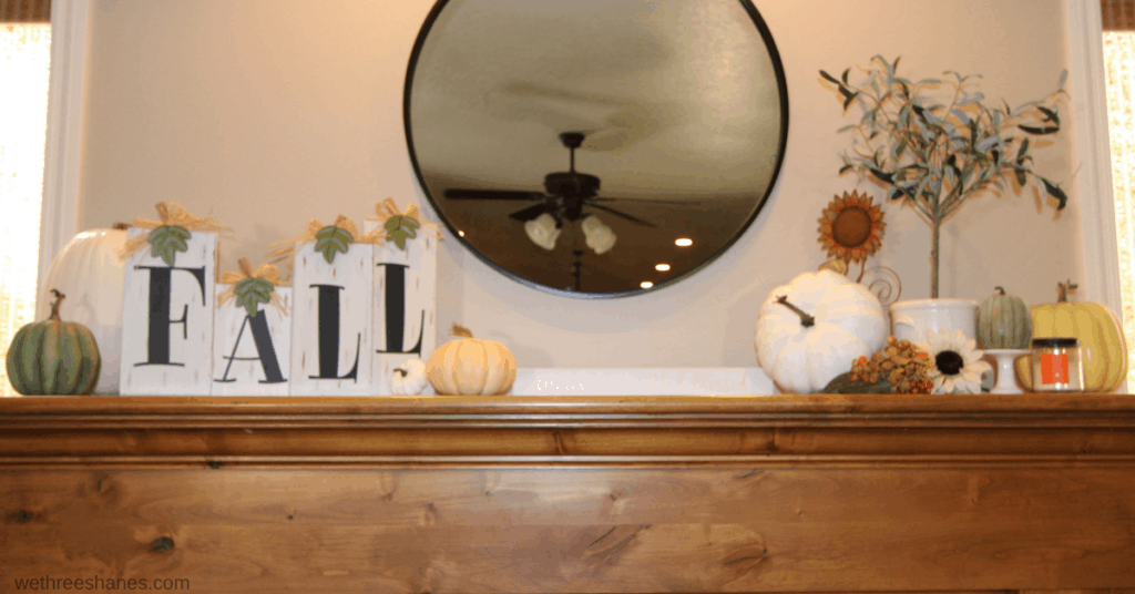 Fall mantel that Fall blocks and pumpkins on one side of a hanging round mirror and pumpkins, an olive tree, and candle balance out the other side.