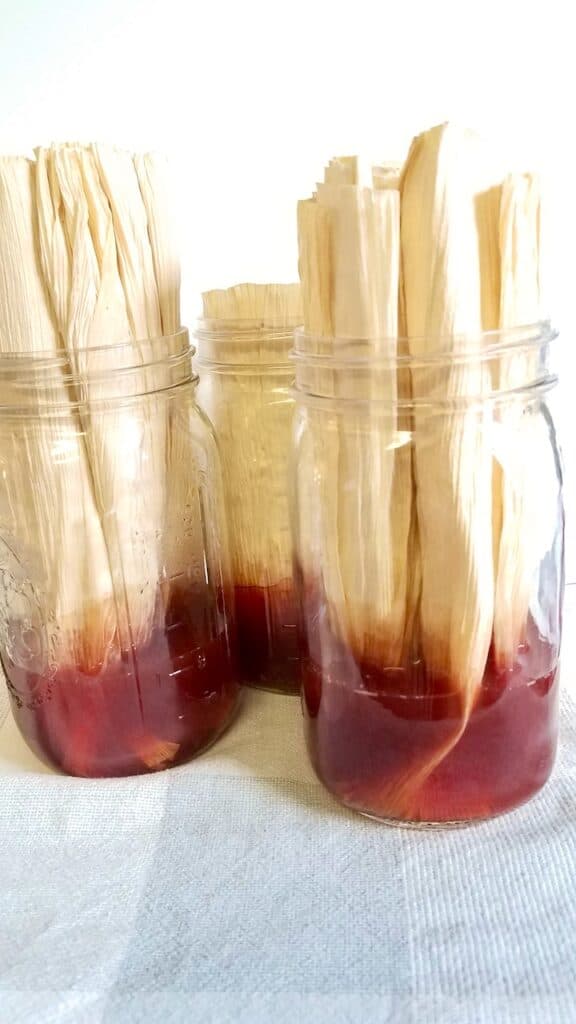 Corn husk sits in ball jars full of red-brown natural dye made from avocados.