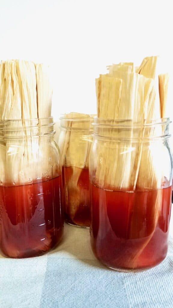 Corn husk sits in ball jars full of red-brown natural dye made from avocados.