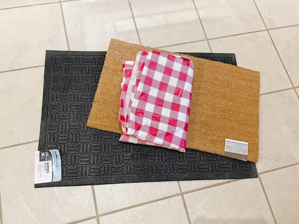 One black 24x36 inch doormat and a 18x30 inch brown mat are used to make a layered mat look for the front door. A red buffalo check table cloth is used to make the mat interchangeable.