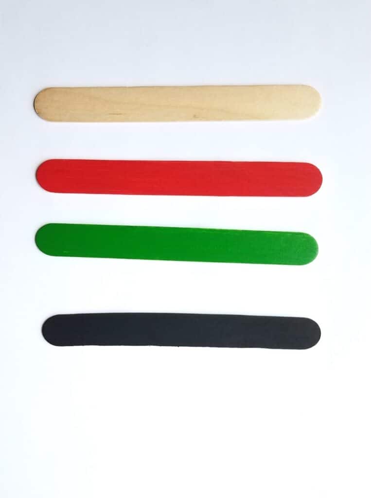 4 popsicle sticks line up one above the other.  The first is neutral. The next is painted bright red, then bright green, and the last one is black.