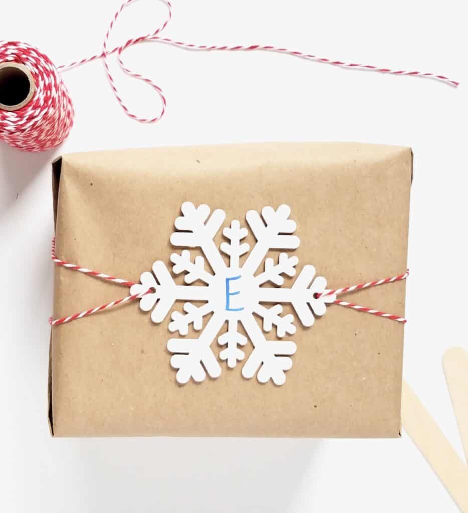 A box wrapped in brown paper with a snowflake gift tag sitting on top being held on by red and white bakers twine.