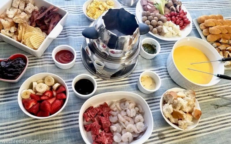 Table spread with a three course fondue, broth, cheese, and chocolate fondue with all the dippings