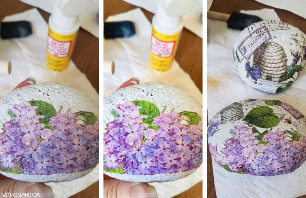 Decoupage rocks tutorial-photo one putting purple flower napkin cut out on the rock with mod podge, photo two same rock with mod podge over the napkins, photo 3 is two rocks fully decoupaged with garden scene napkins and set aside to dry.  