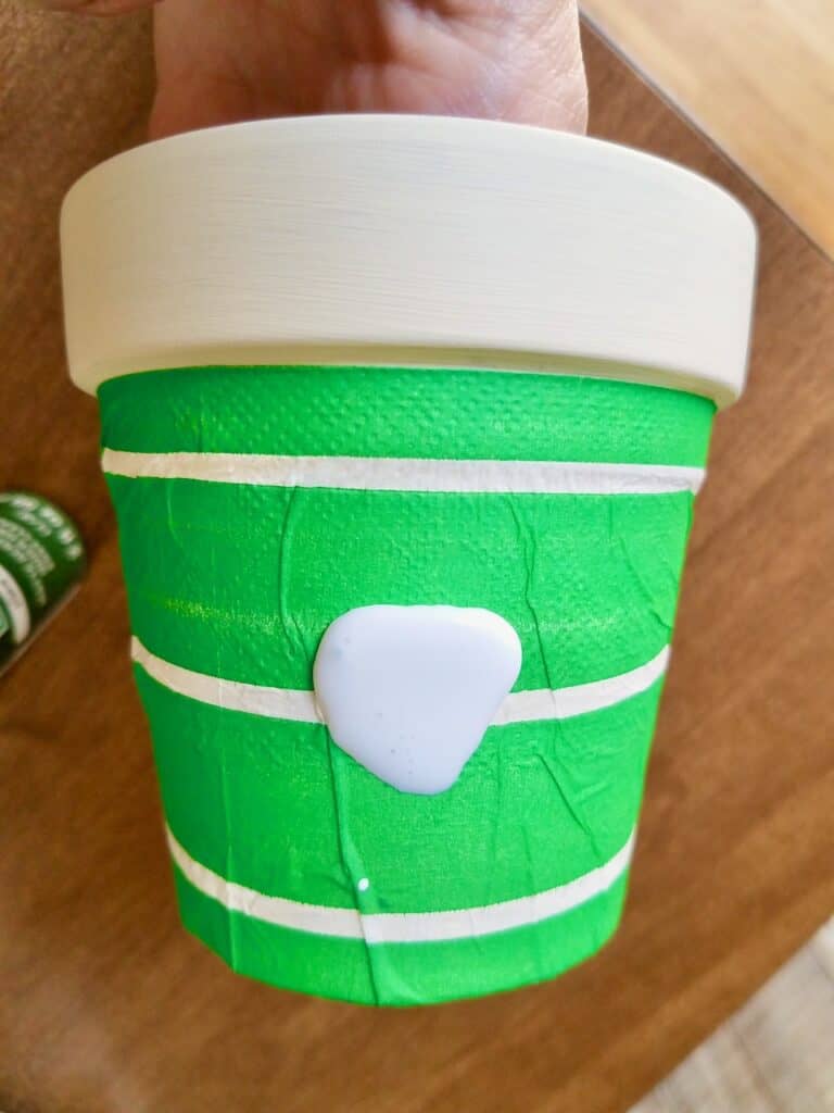 A cream color painted terra cotta pot has a bright green and white stripe napkin being decoupaged onto it.