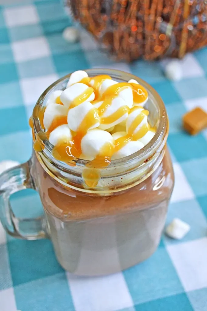 Clear mug of hot cocoa topped with mini marshmallows and drizzled with caramel 