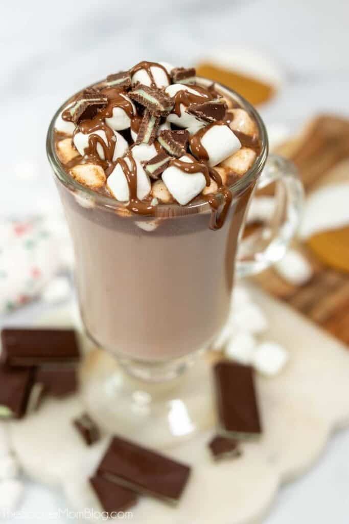 Hot chocolate in a clear mug, topped with mini marshmallows, broken up andes mints, and drizzled in chocolate syrup.