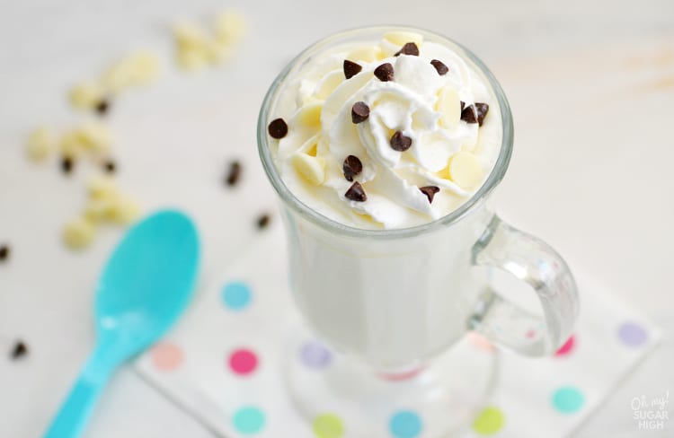 White hot chocolate in a clear mug topped with shipped cream and chocolate chips 