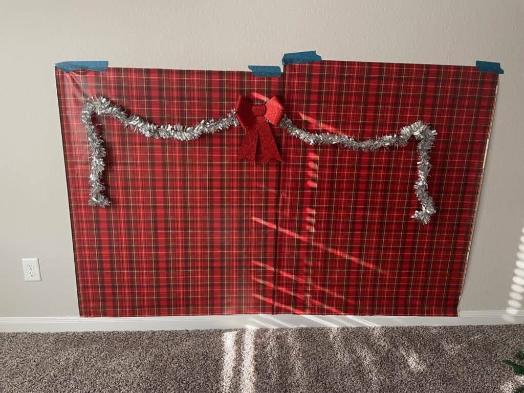 Christmas wrapping paper taped to a wall with some tinsel garland and a red glitter bow