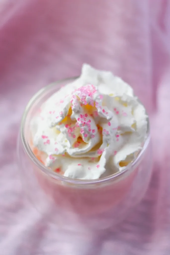 Pink Hot Chocolate in a clear glass, topped with whipped cream and pink sprinkles