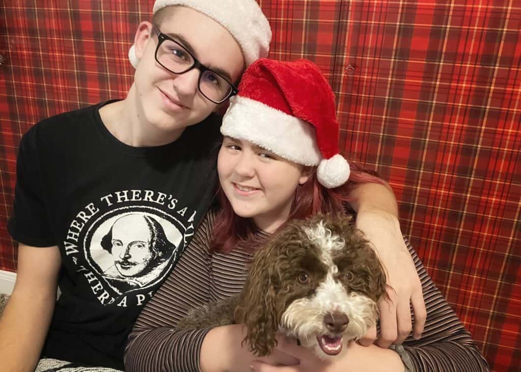 A teenage boy and teenage girl both with Santa hats on their heads.  They are smiling and holding a puppy