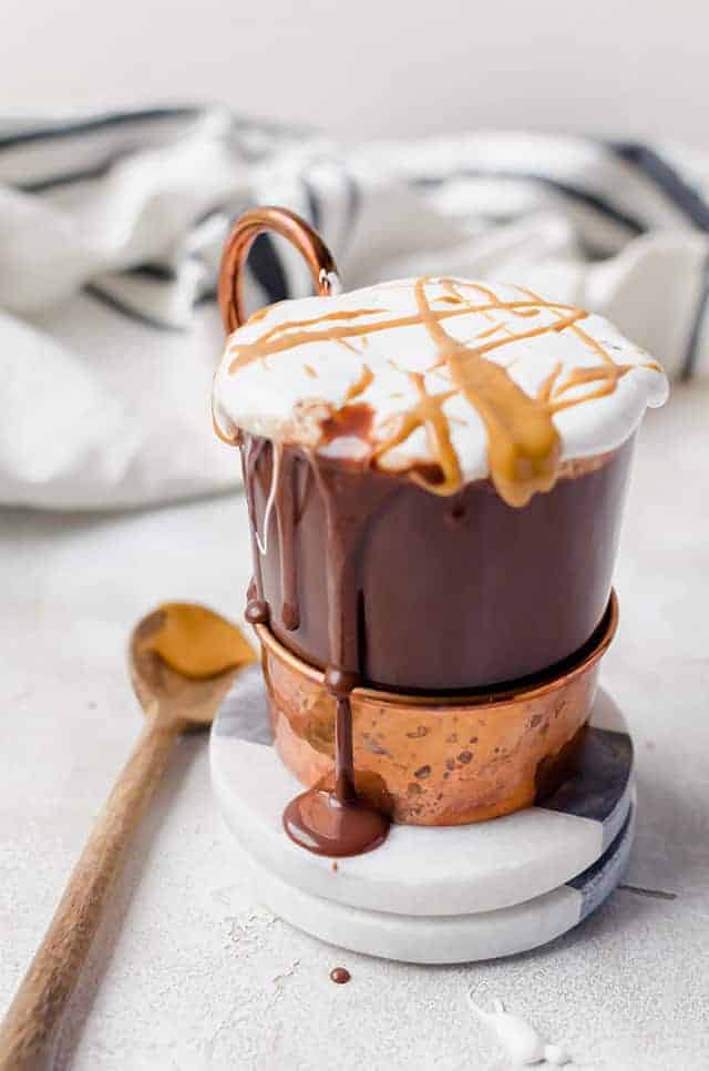 Mug of hot chocolate topped with whipped cream, drizzled in peanut butter.