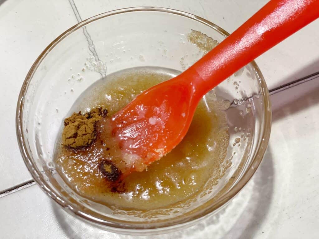 Close up picture of sugar scrub ingredients in a glass bowl with a orange spoon