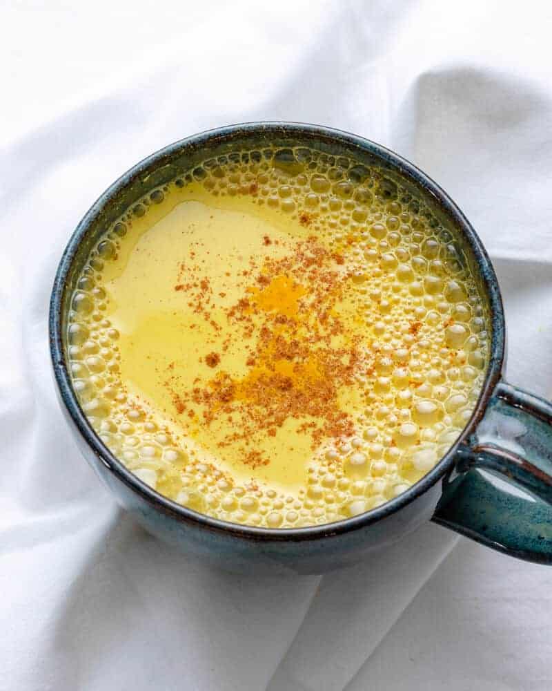 Dark mug full of bright yellow liquid with cinnamon sprinkled on top.