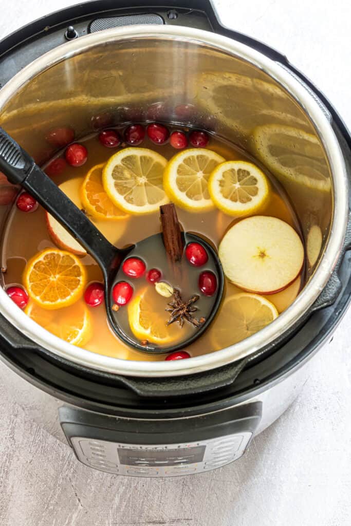 Instant pot of mulled cider with apple and orange slices, cinnamon sticks, and cranberries.