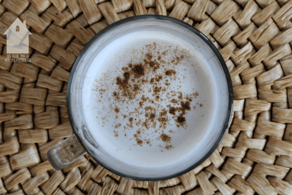 Over view shot of white drink in a clear mug with cinnamon sprinkled on top.