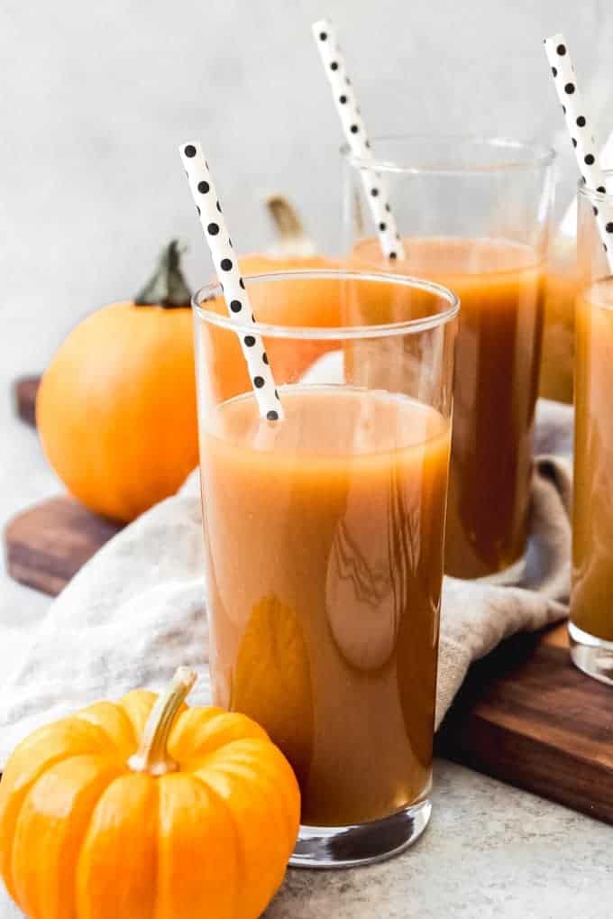 Clear tall glass filled with pumpkin juice with white and black polk-a-dot straw in cup.