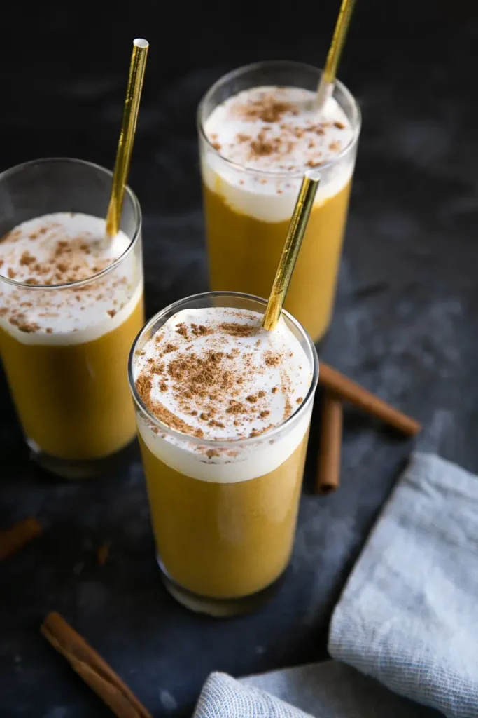 3 tall clear galsses filled with pumpkin smoothies, topped with whipped cream and cinnamon.