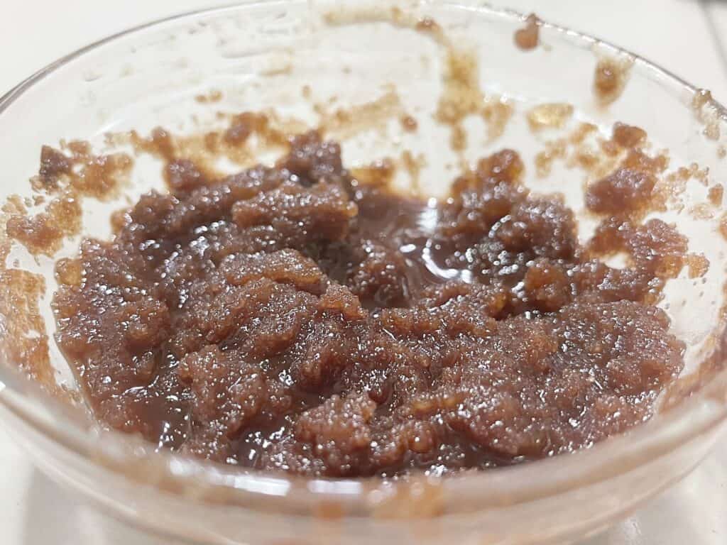 Up close picture of some brown sugar mixed with almond oil in a glass bowl