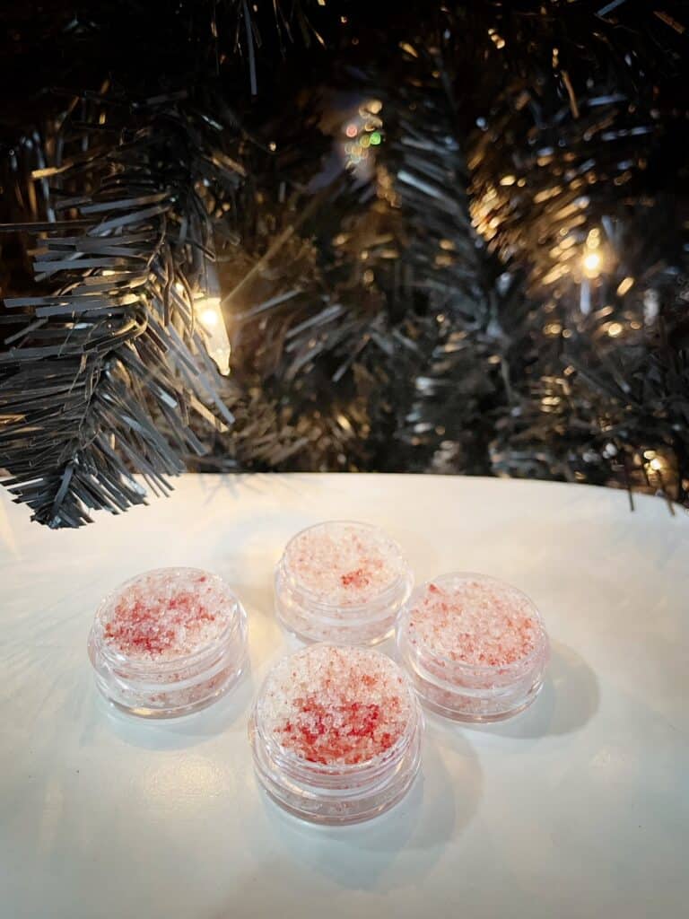 4 lip scrubs with white and red sugar next to a Christmas tree