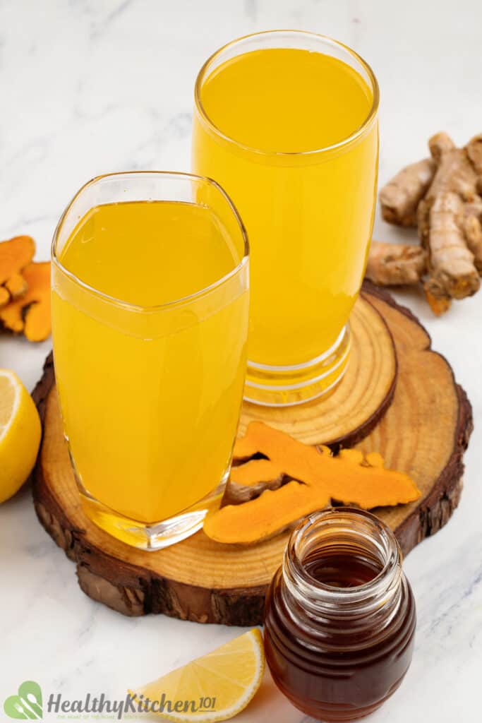 Bright yellowish-orange drinks in tall, clear glasses sitting on a slab of log.