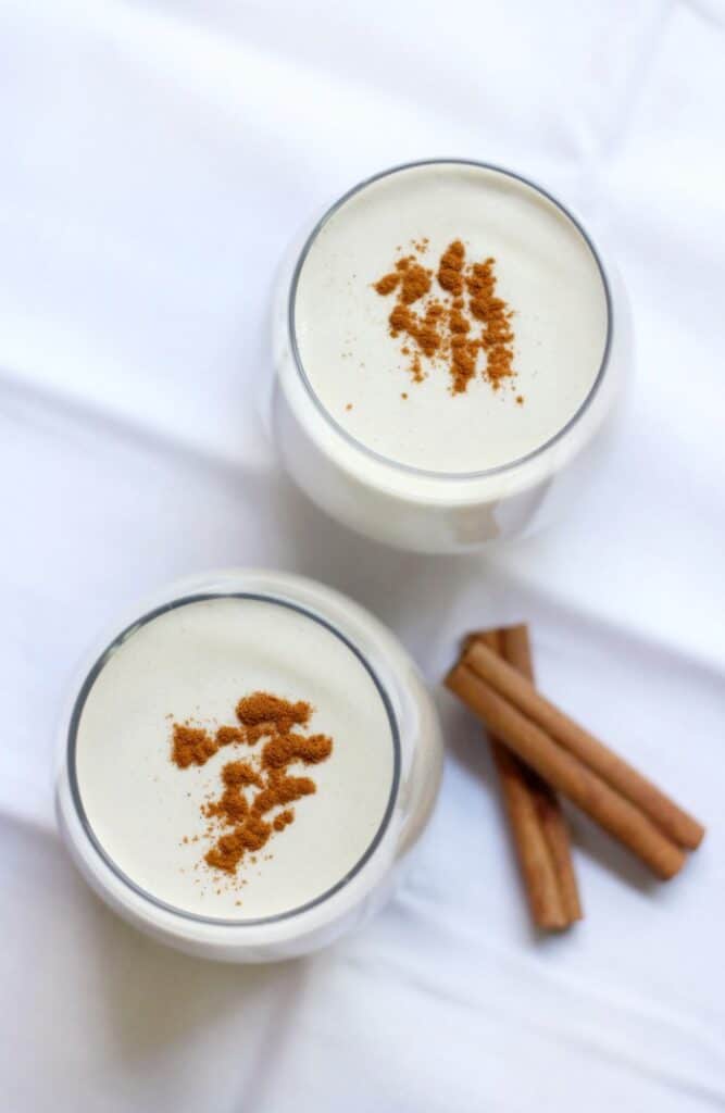 Two glasses of vegan eggnog on a white table.