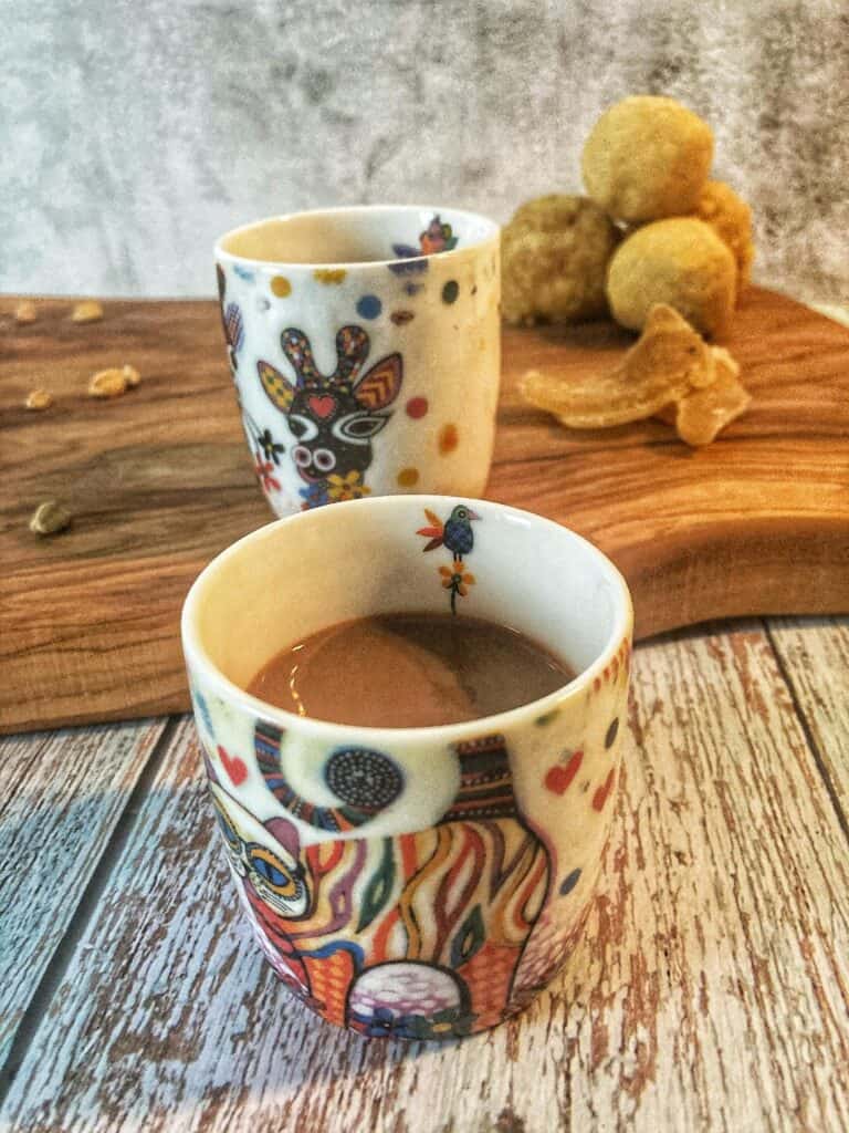 Dark brown tea in colorful animal mugs on a wood table.