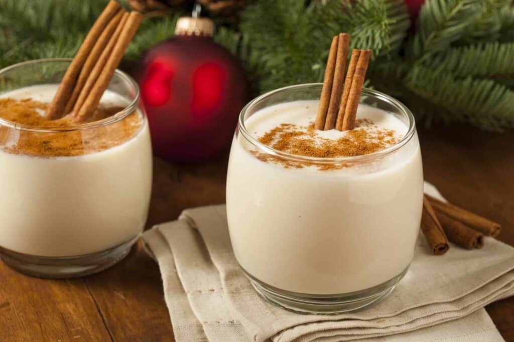 Two cups of homemade eggnog with cinnamon sticks popping out of each cup.