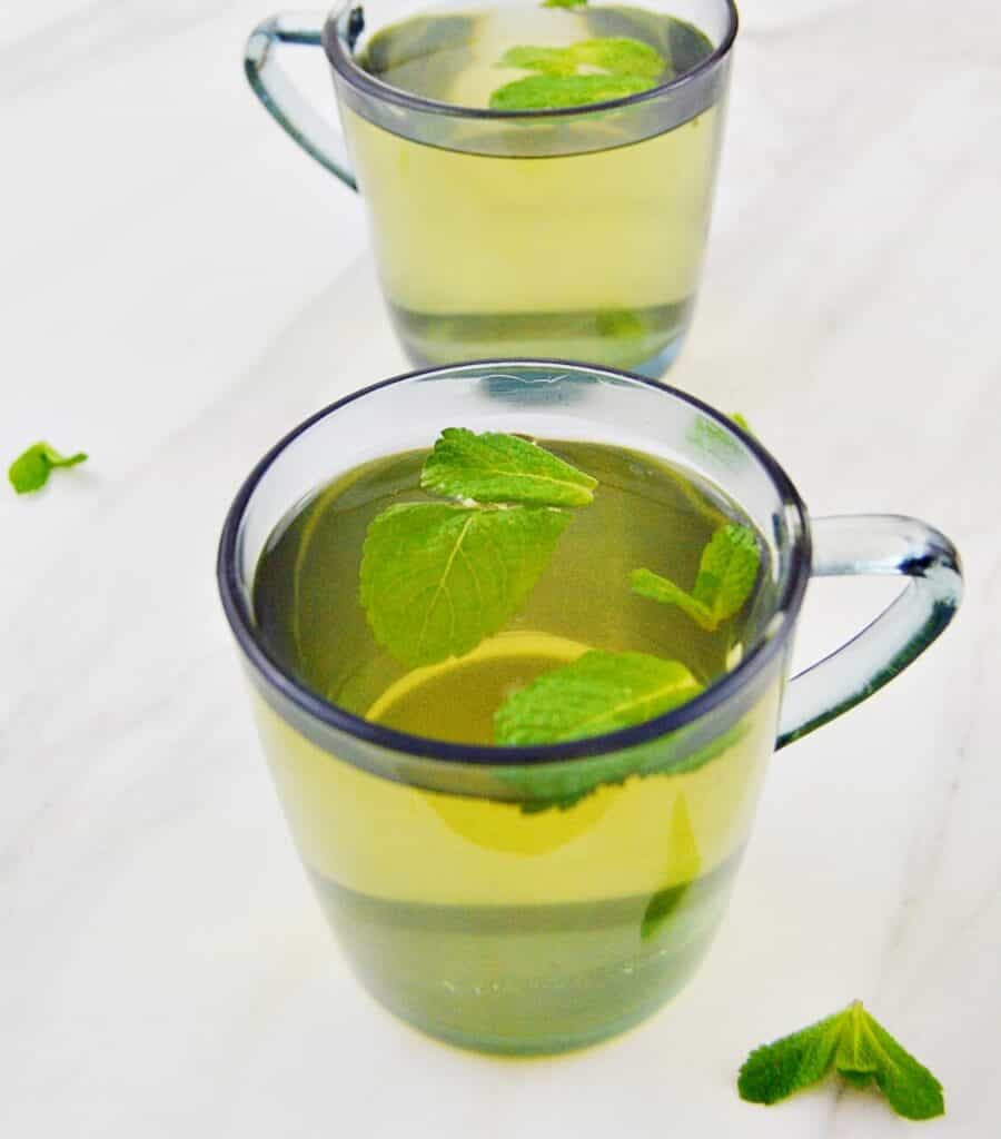 Light green tea in a clear cup with floating mint leaves.