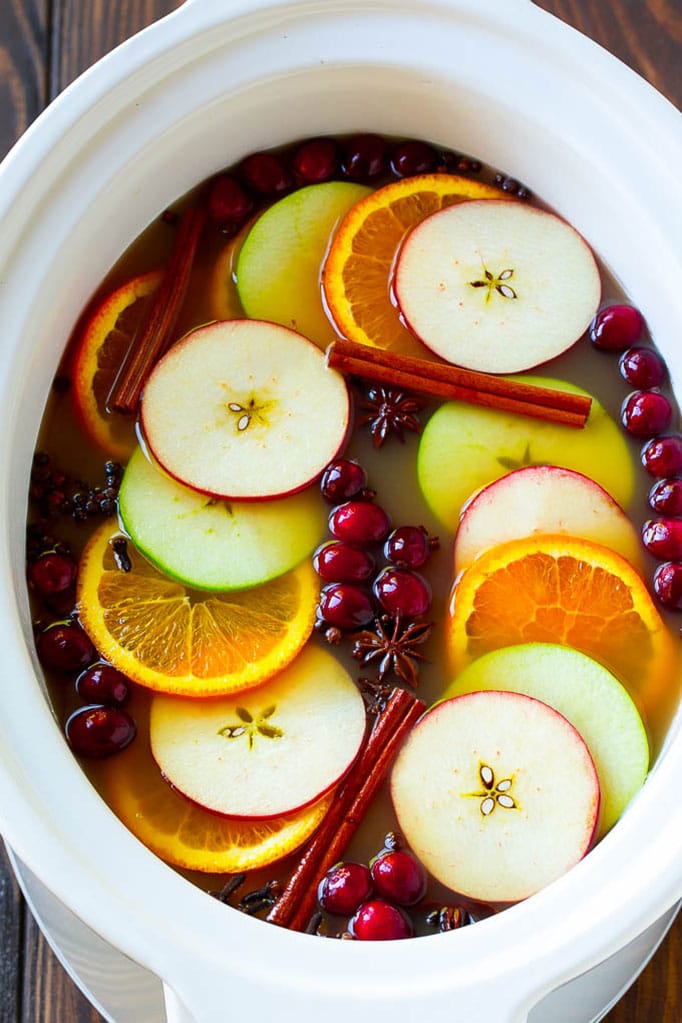 Crockpot full of cider, apple and orange slices, cranberries, cinnamon sticks, and cloves.