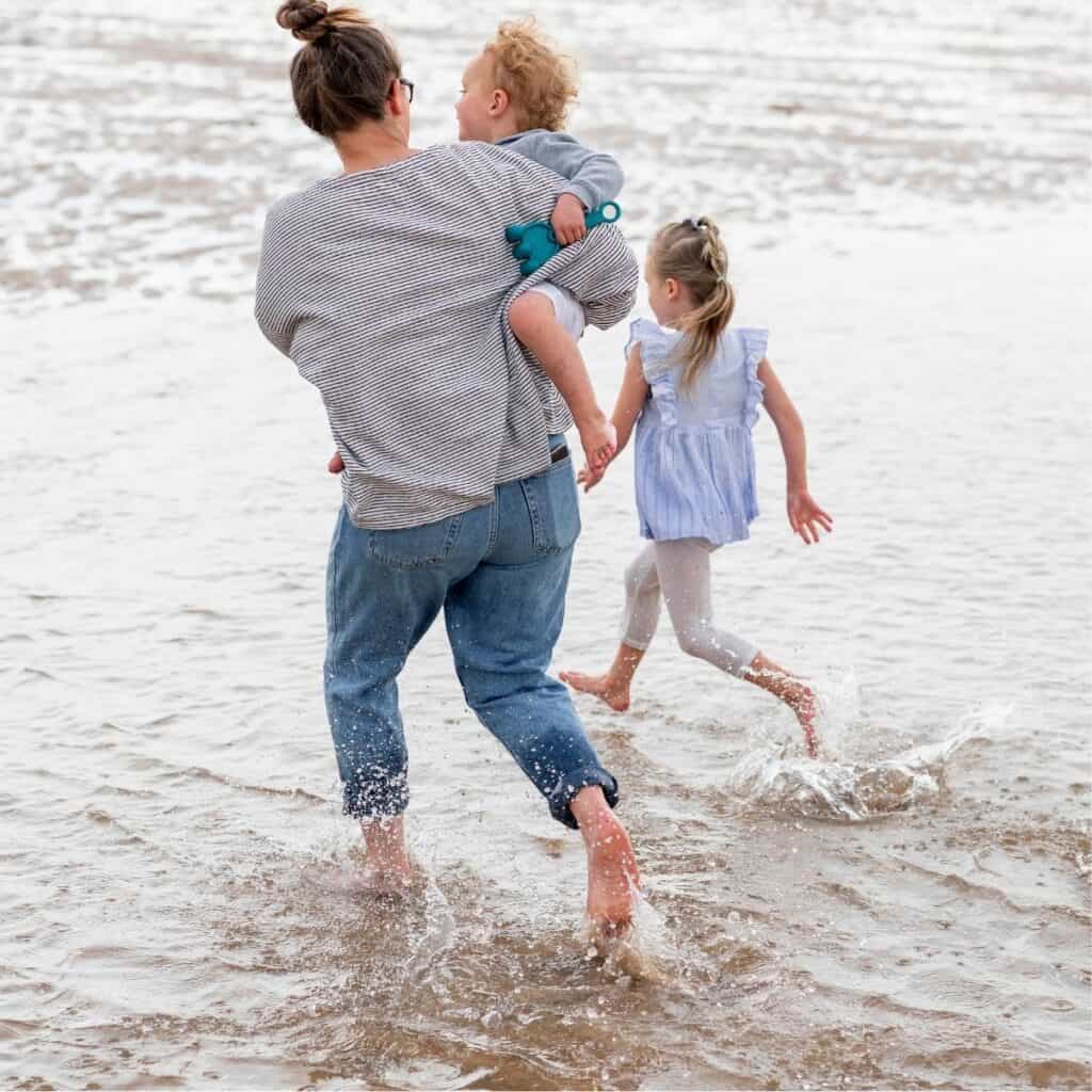 Mom and two young kids running into the water together.