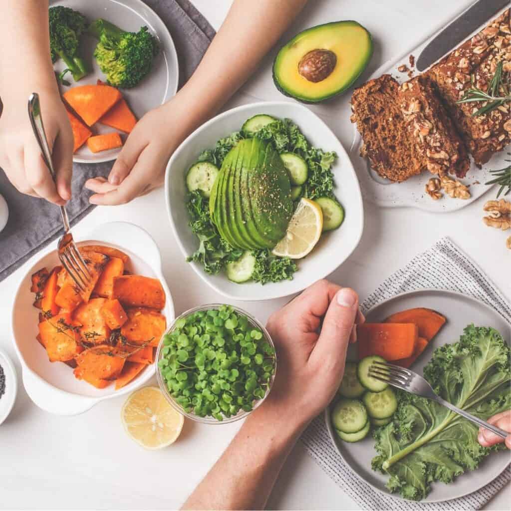 Hands of two people serving up a table full of healthy foods.