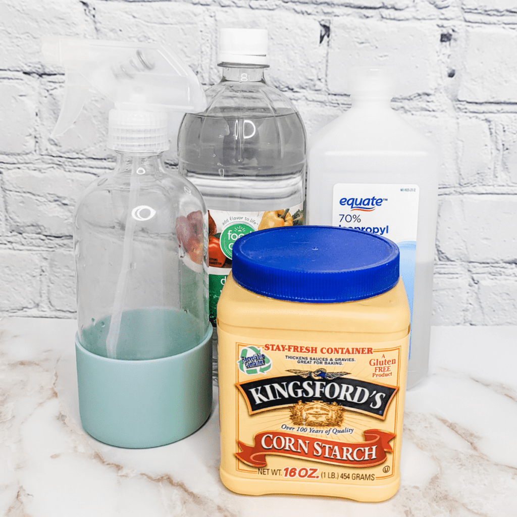 Ingredients in our amazing DIY glass cleaner, a bottle of vinegar, rubbing alcohol, and corn starch, with a reusable spray bottle.