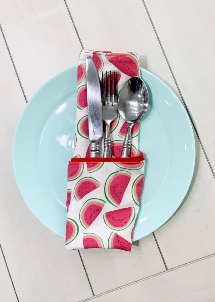 turquoise plate sitting on a table with a cloth napkin with watermelons on the fabric folded with utensils in it | wethreeshanes.com 