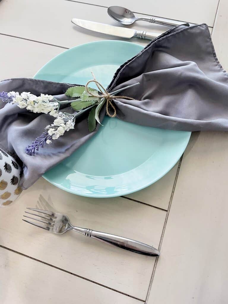 picture of a turquoise plate on a table with silverware and a grey cloth napkin on top of the plate | wethreeshanes.com