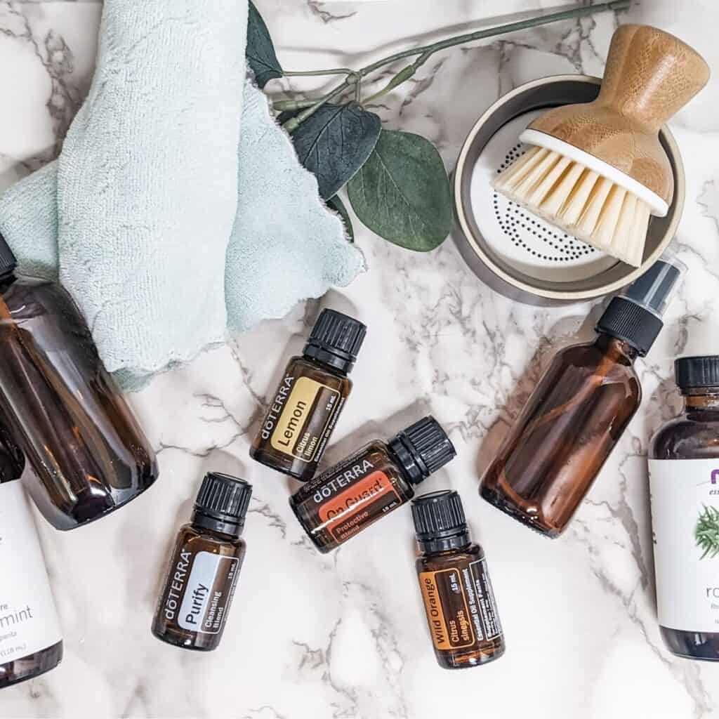 The best Essential Oils for cleaning. A bunch of essential oils laying on a white marble counter with some cleaning supplies.