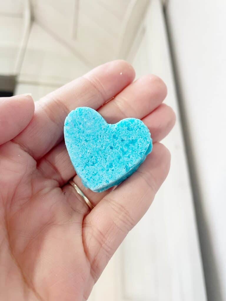 A hand holding a blue heart shaped bath bomb