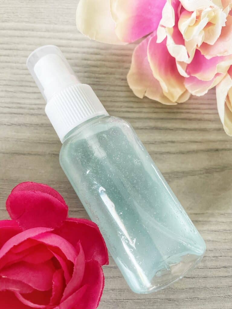 picture of a spray bottle with light blue water and two how pink flowers next to it