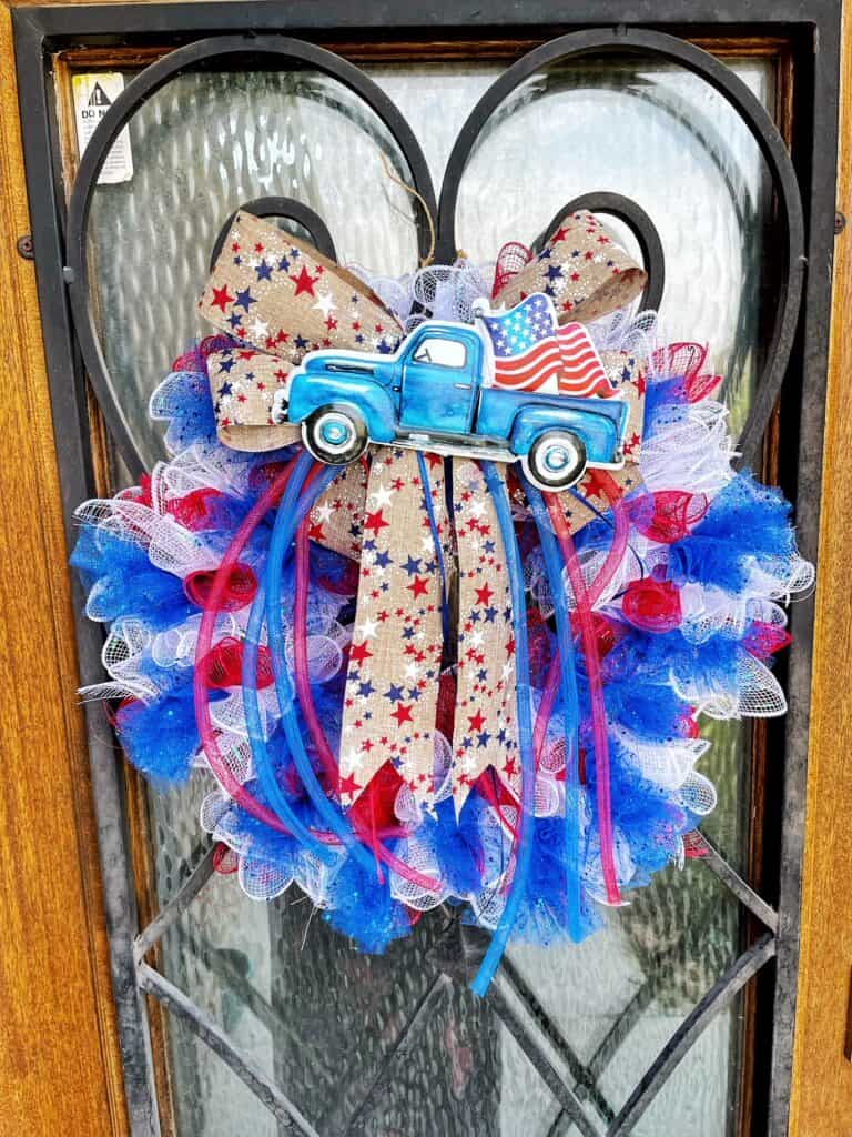 Finish wreath hanging on a front door.  Red, White and blue deco mesh and a ribbon with stars and a blue metal truck