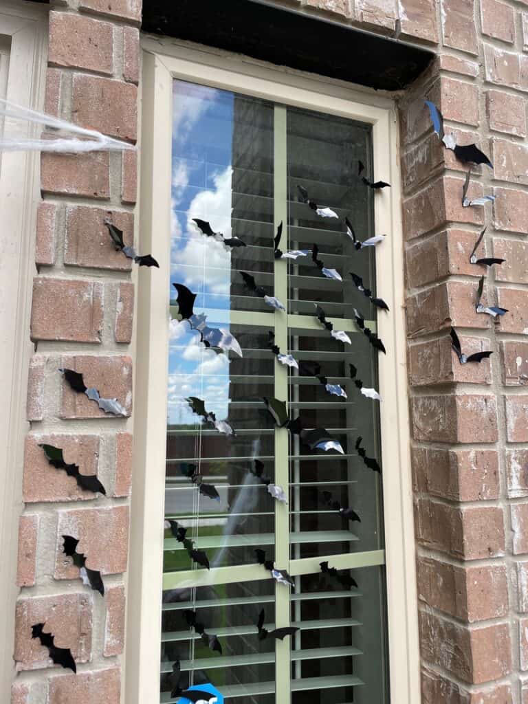 A bunch of plastic halloween bats stuck to a window on the front porch of a house 