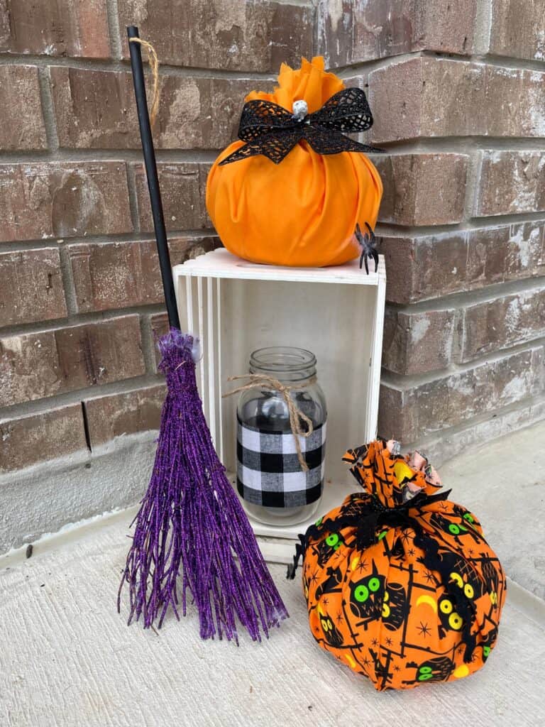 picture of a crate with fabric pumpkins, a witches broom and a mason jar with a candle in it