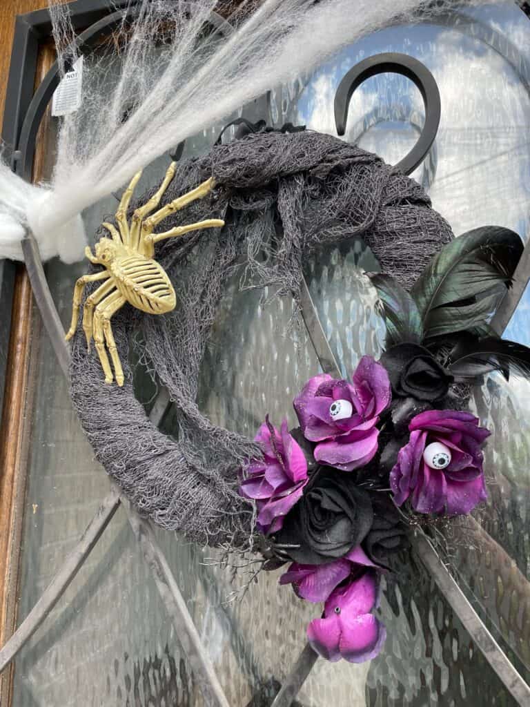 a halloween wreath with a spider, purple and black flowers, some fake eye balls and feathers 